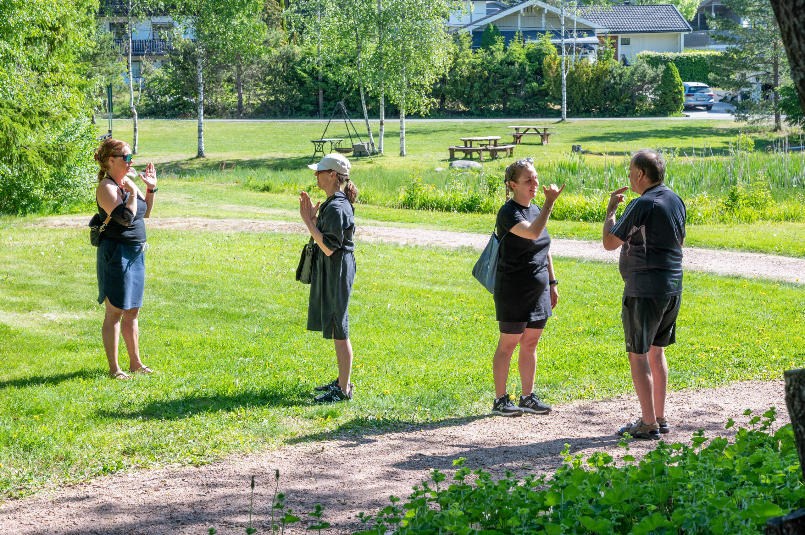 Fire personer står utendørs. De kommuniserer på Norsk tegnspråk.