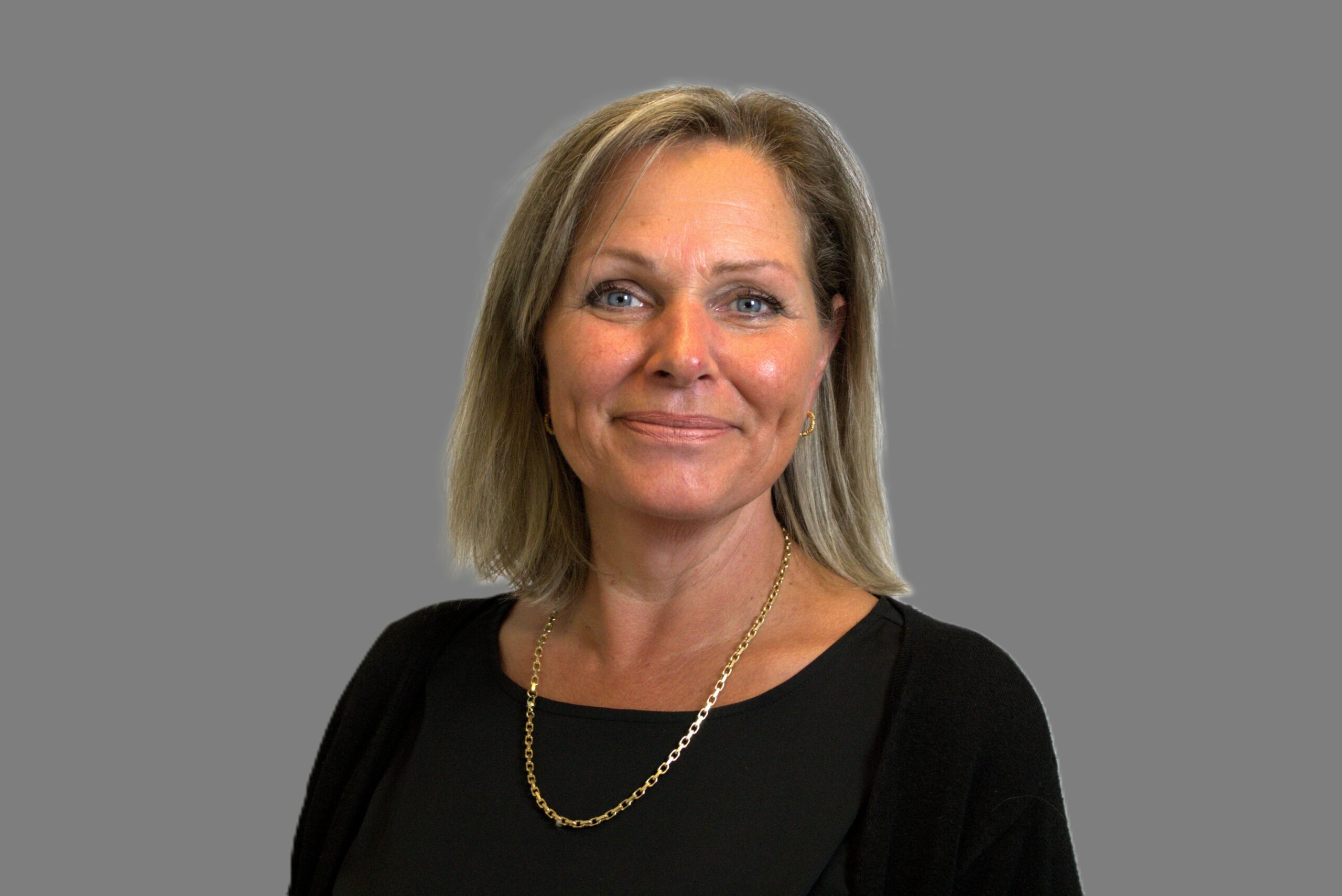 Portrait of Hilde with shoulder-length blonde hair, dark jumper and necklace.