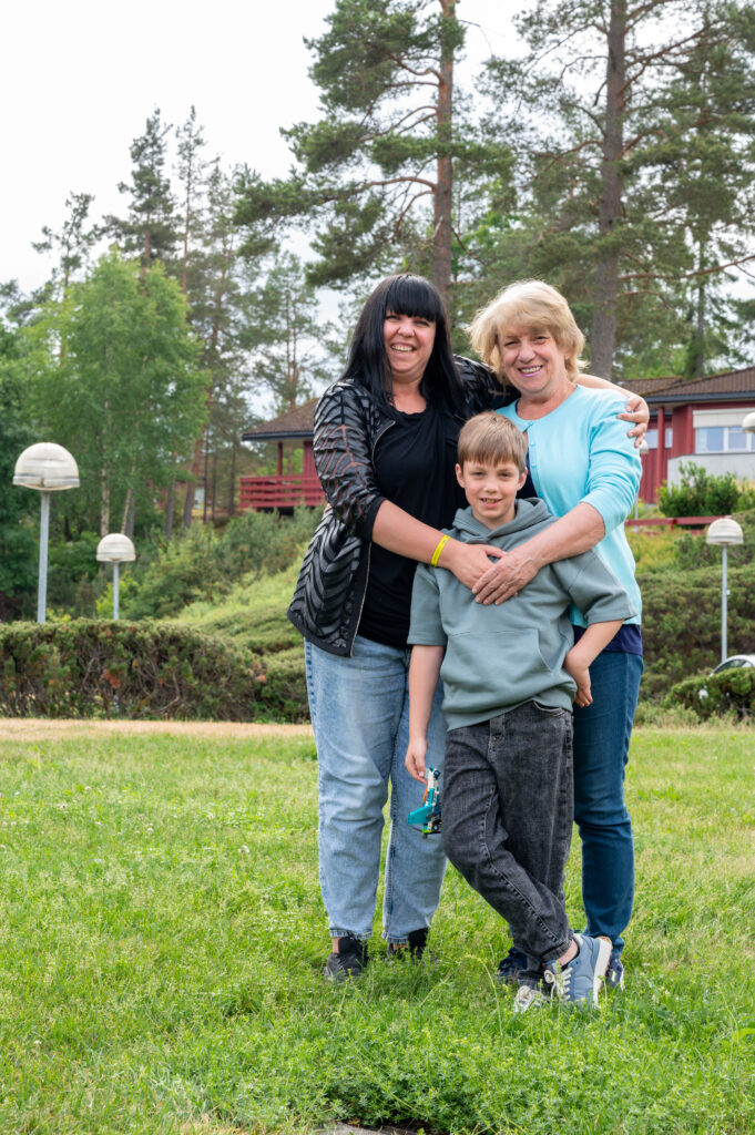 Tre personer står utendørs og holder rundt hverandre.