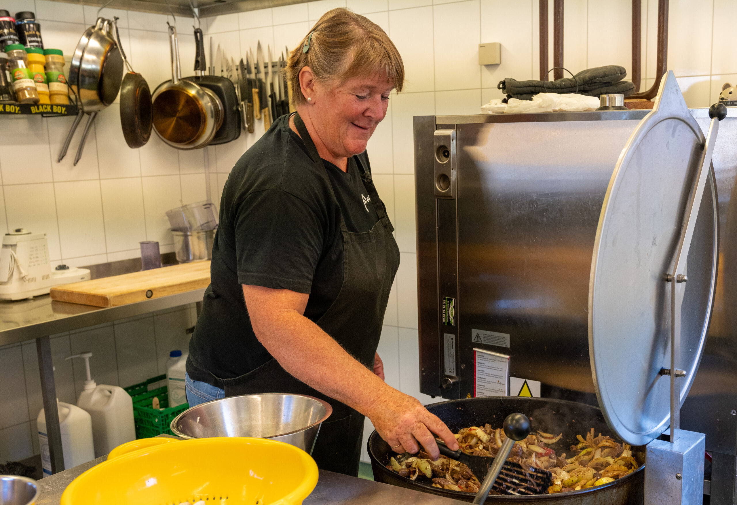 Turid stands by a large pan and cooks food