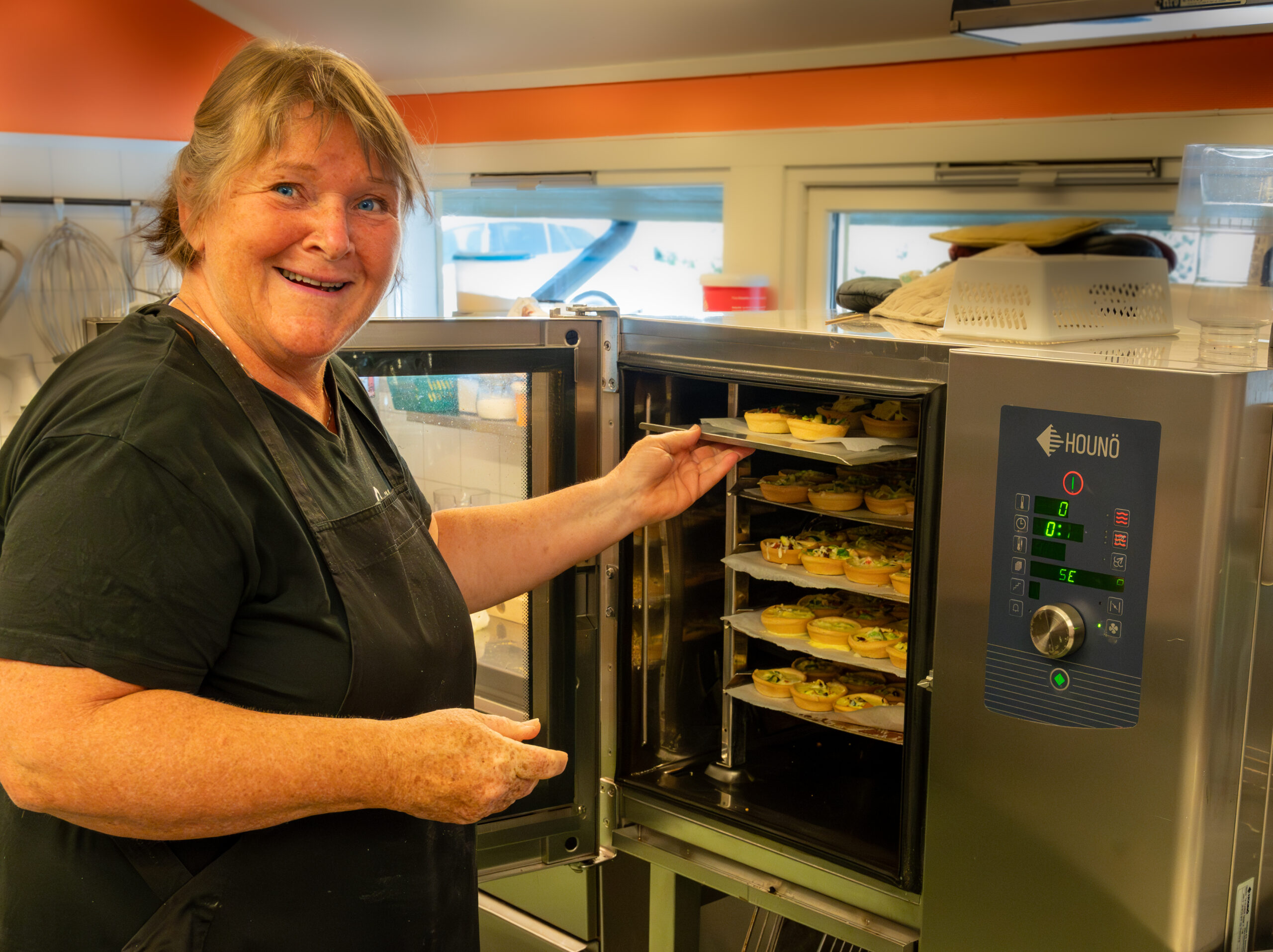 Turid stands by the oven with trays of food