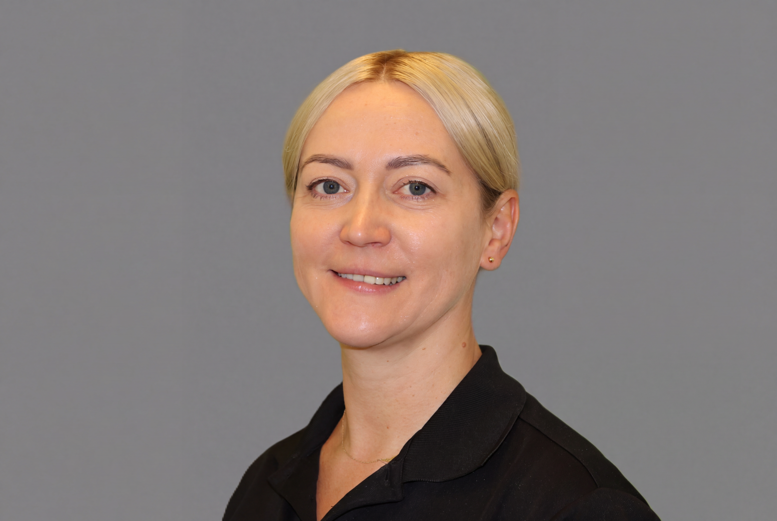 Portrait of Jolanta. She is sitting slightly angled and smiling. She has short, light hair and a black t-shirt.