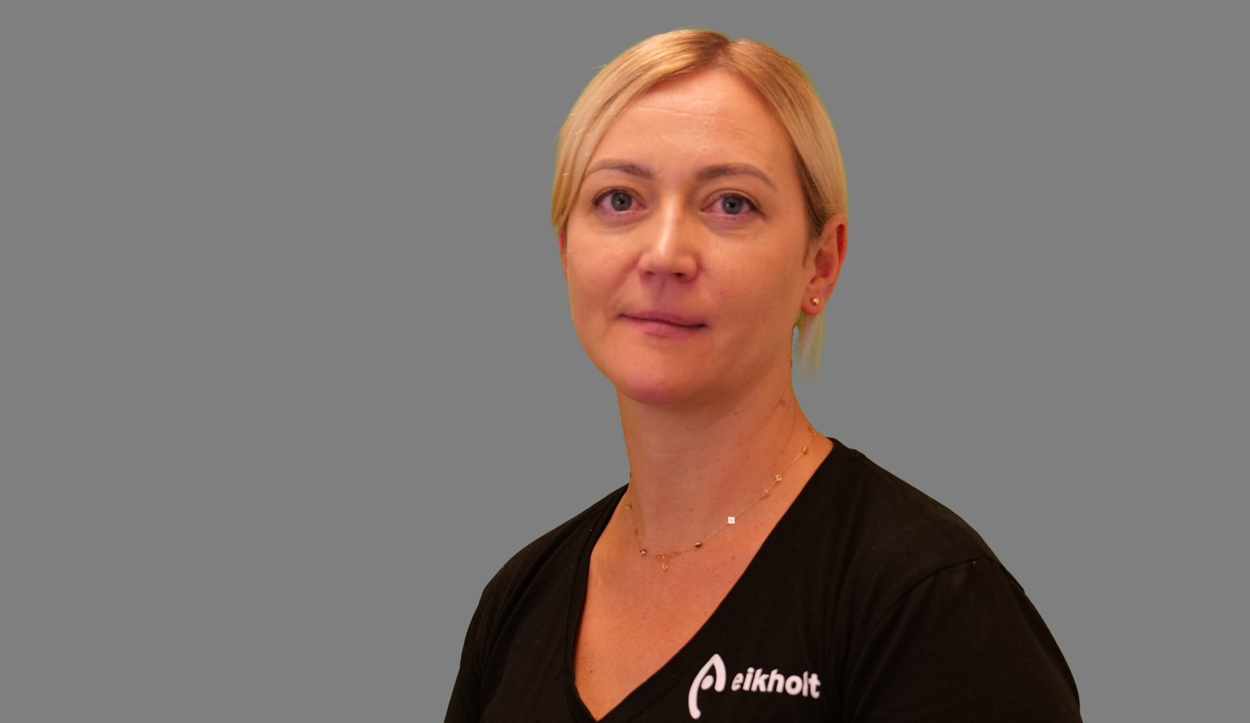 Jolanta has blonde hair down to her ears with a centre parting. She has dark eyebrows and is wearing a black t-shirt.