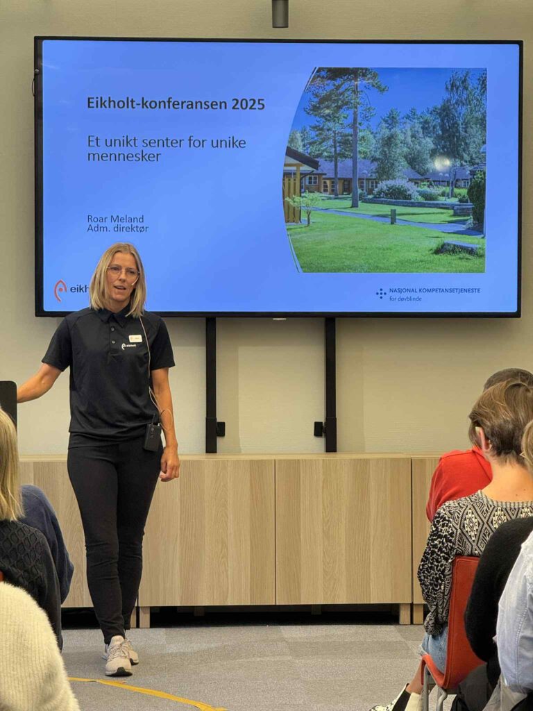 Tanja Teigum står foran en skjerm. Hun holder en hånd på en talerstol.