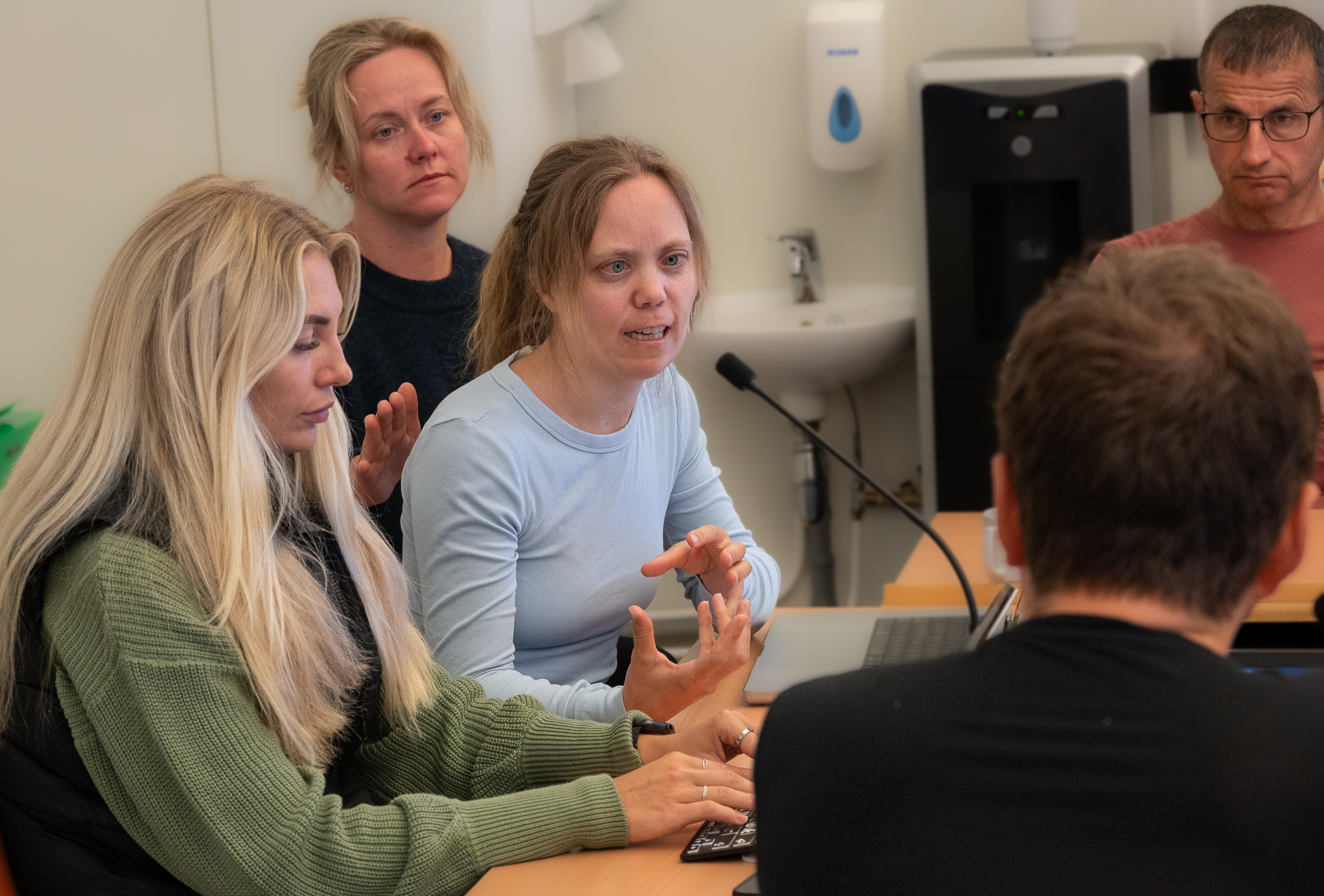 En person snakker i mikrofon og får haptisk signal på ryggen. En skriver på et tastatur og to sitter og lytter.