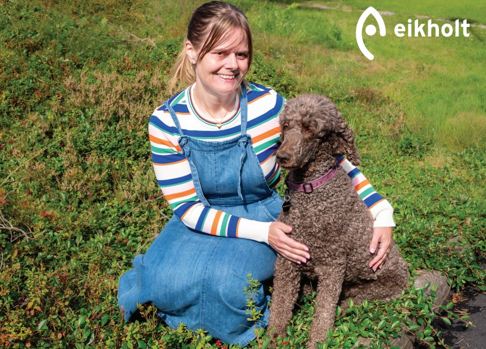 En dame og en hund sitter i lyngen. I hjørnet står det Eikholt