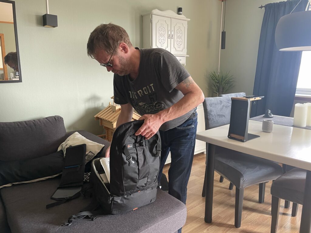 Pål Kjetil tager teknisk udstyr op af en sæk. Sækken står på en sofa. Bag ham står et bord og nogle stole. På bordet står en holder med VoxiVision.