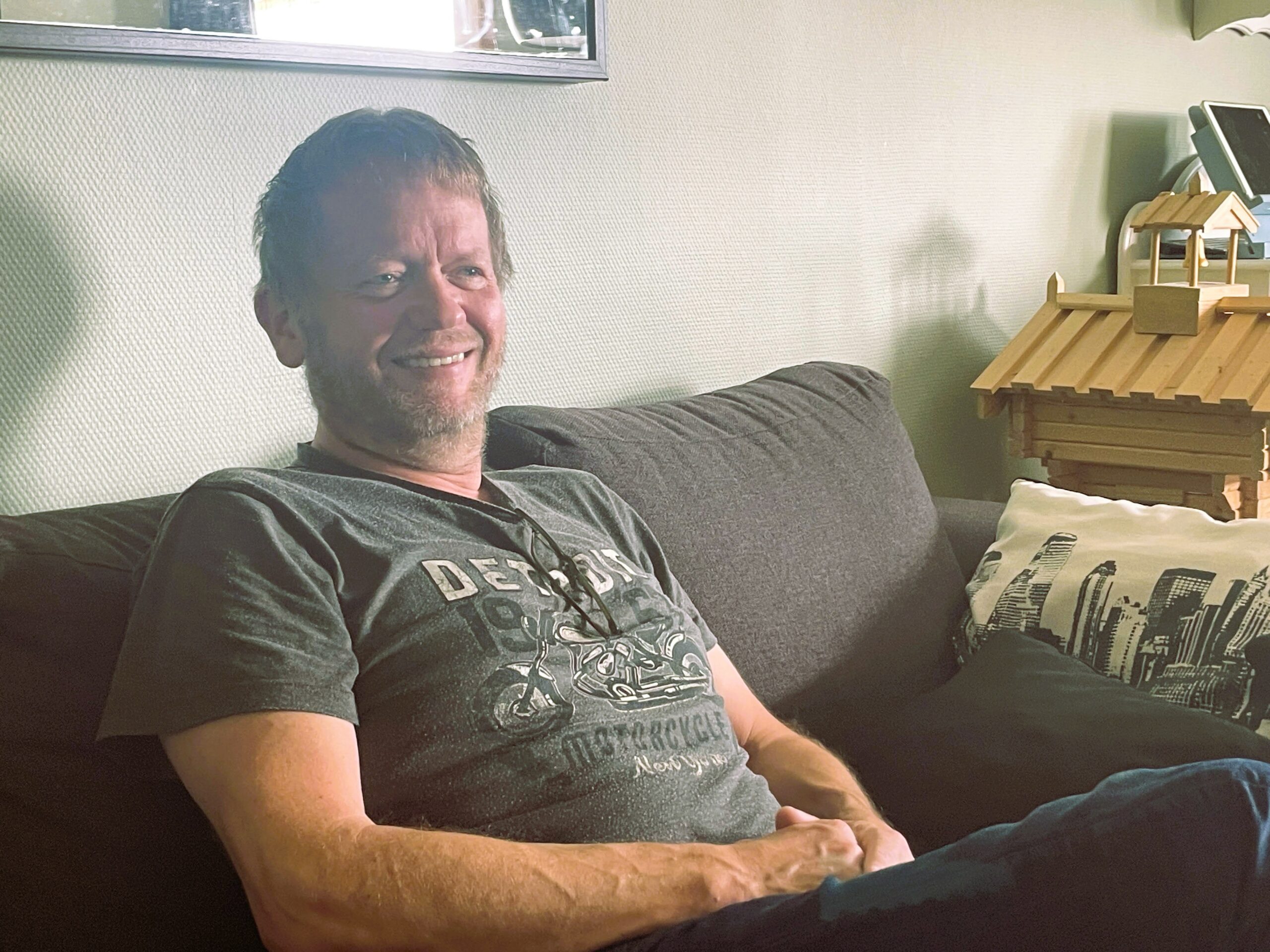 Pål Kjetil sidder i en sofa. Han har kort hår, smiler og er iført en grå t-shirt.