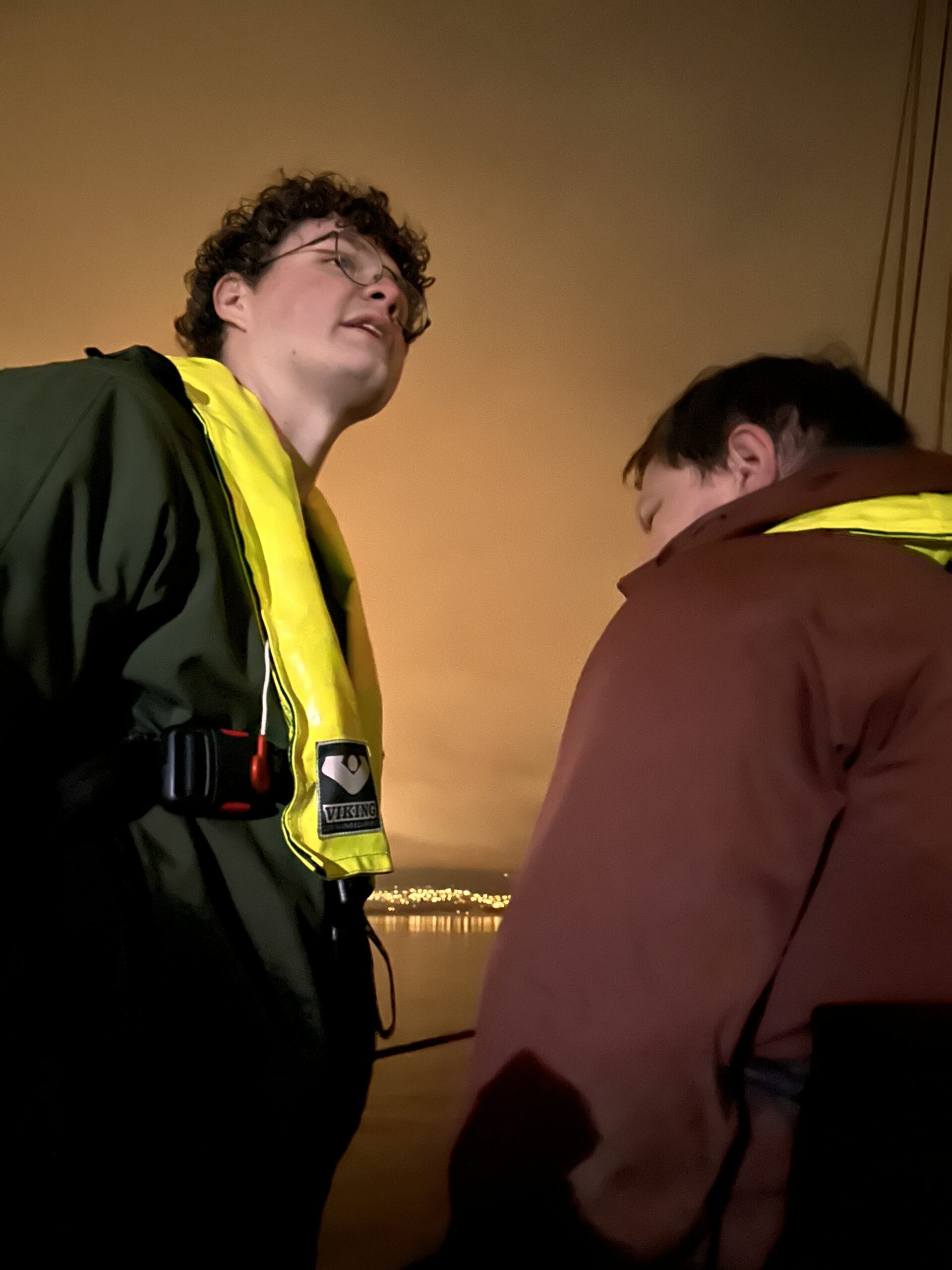 To personer står ude med redningsveste. Det er mørkt, men lyst længere tilbage.