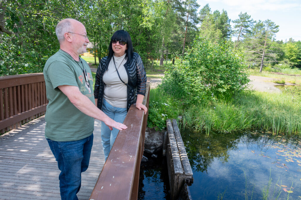 To personer står ute på en bro. En person har på en rogerpenn, den andre personen hatt briller og hørapparat.