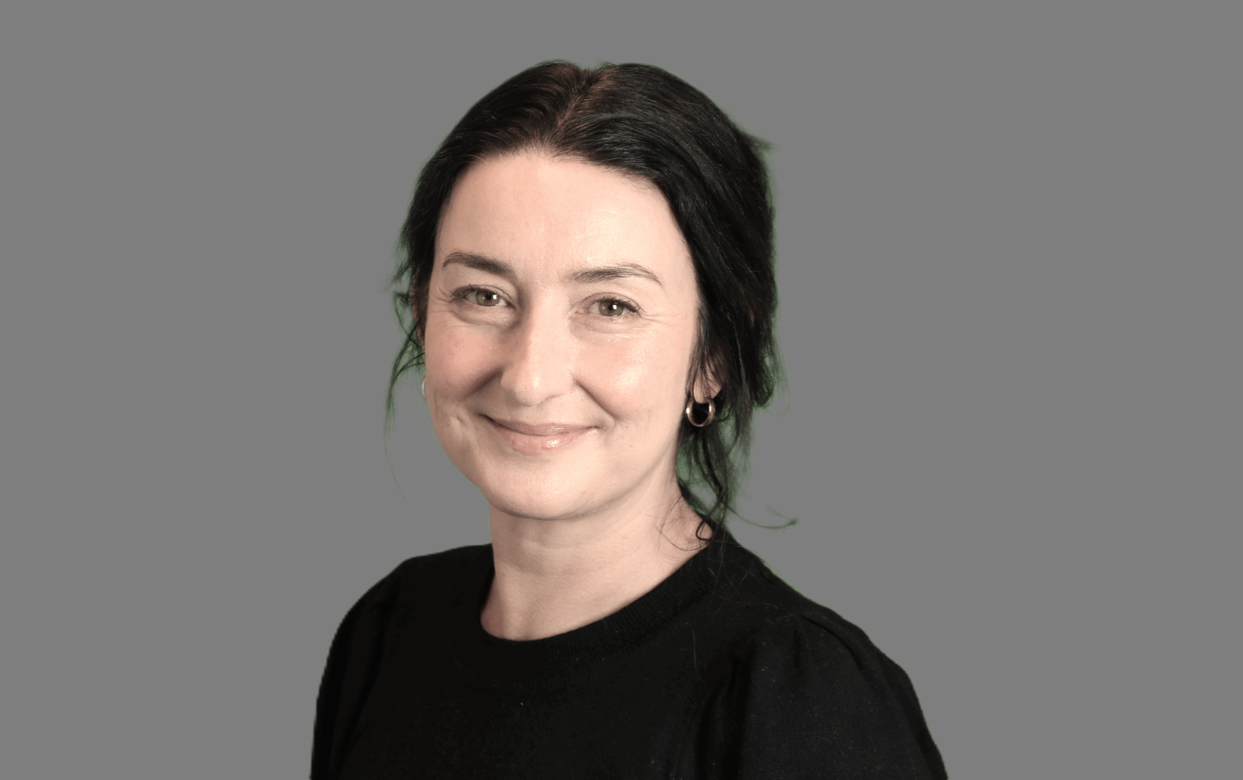 Portrettbilde av Gøril. Hun har sort oppsatt hår, hun har mørke øyebryn og brune øyne. Bruker øredobber og smiler med lukket munn.