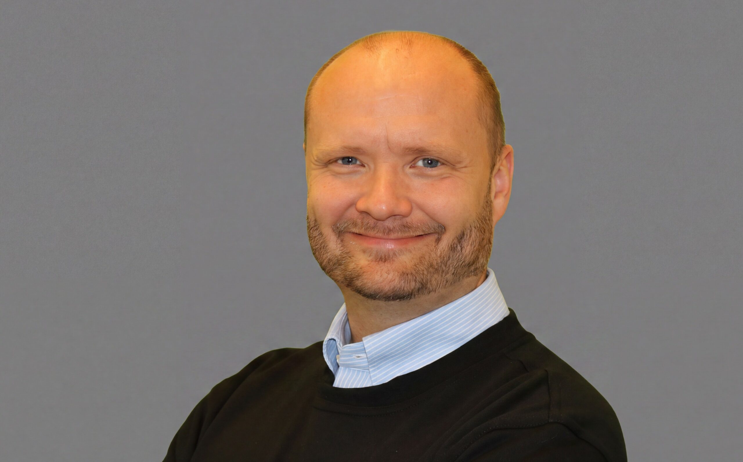 Ben-Lewi har kort hår og lett skjegg. han bruker en lys skjorte under mørk genser og smiler mot kamera.