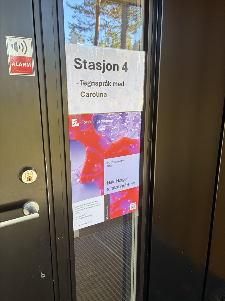 Skilt på en dør: "Station 4 – Tegnspråk med Carolina", med plakater til Forskningsdagene den 16. til 27. september 2026