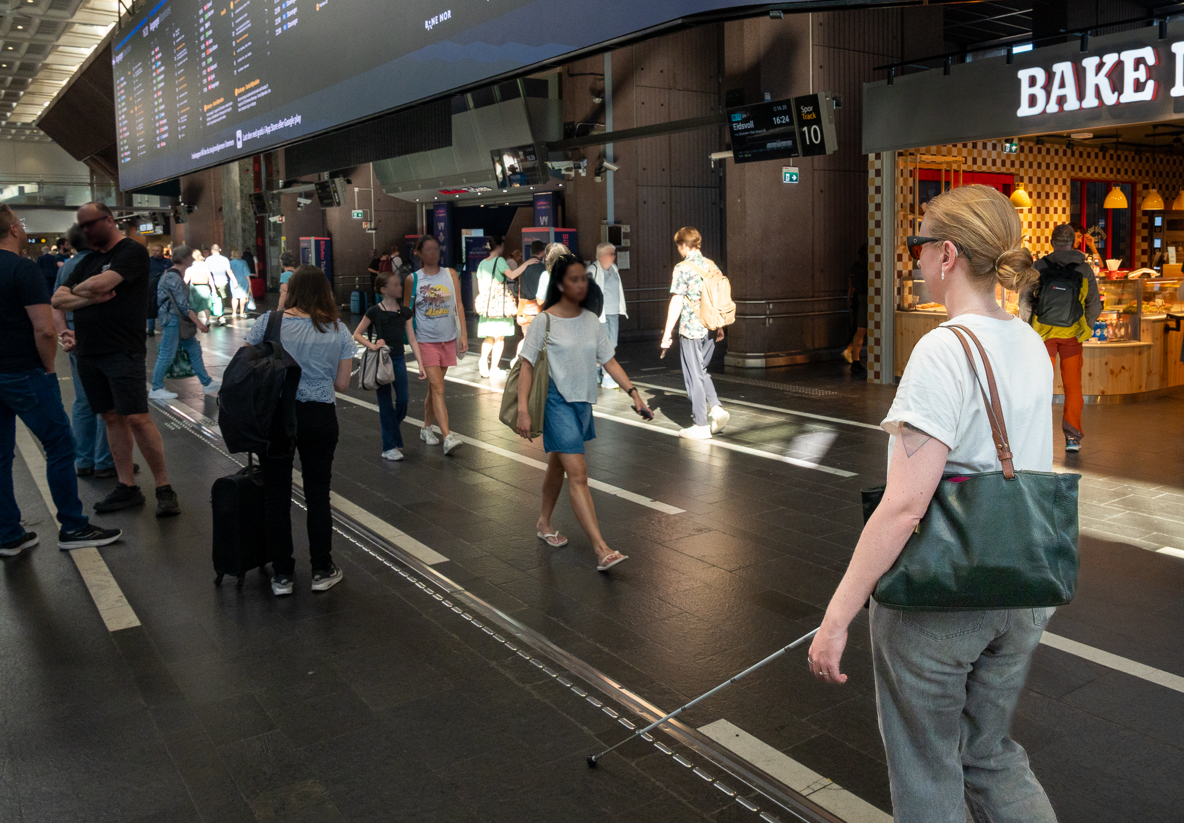 En kvinde går på Oslo Central Station. Hun har sat håret, en taske og en hvid stok og følger en rutevejledning.
